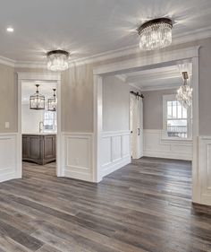 an empty living room with hard wood floors and white walls, chandeliers on the ceiling