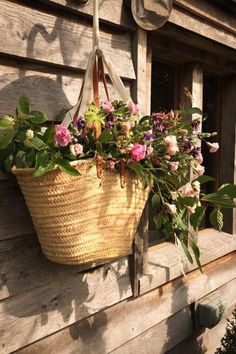 a basket filled with flowers hanging from the side of a wooden house window sill