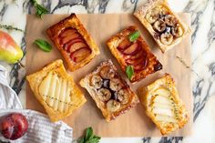 several desserts are arranged on a cutting board next to an apple and mint garnish