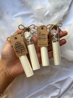 three white candles are tied with twine and labeled merry christmas messages on them, sitting in front of a white sheet