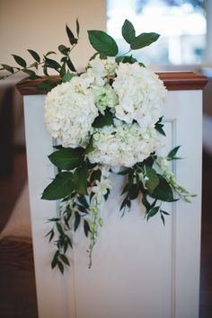 white flowers and greenery are on the back of a church pew