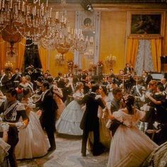 a group of people dressed in formal wear dance around a chandelier filled room