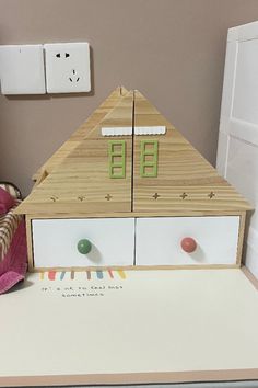 a toy house made out of wood and white drawers on top of a table next to a stuffed animal