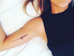 a woman laying in bed with a tattoo on her arm that reads w and has an arrow