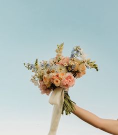 a bouquet of flowers being held by someone's hand against a blue sky background