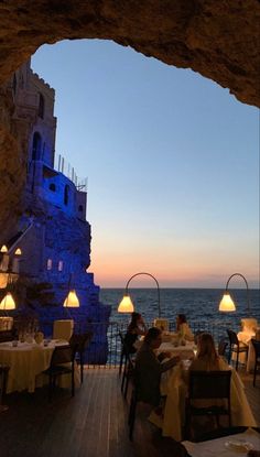 people are sitting at tables in front of the ocean and an archway leading to a restaurant