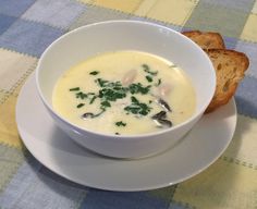 a white bowl filled with soup next to a piece of bread on a tablecloth