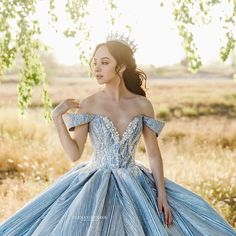 a woman in a blue and white dress standing under a tree with her hands on her hips