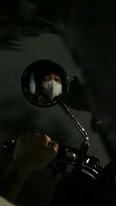 a person wearing a face mask while riding a motorcycle at night with their reflection in the side mirror