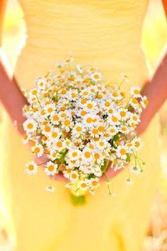 a woman holding a bouquet of daisies in her hands