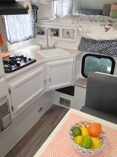 the interior of a camper with fruit in a bowl on the kitchen table and sink