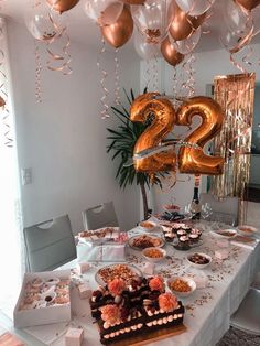 a table topped with lots of desserts and balloons in the shape of two twenty