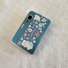 a cell phone case sitting on top of a white tablecloth covered bed sheet with an elephant and flowers design