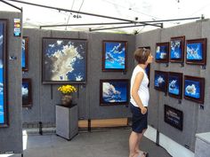 a woman is looking at paintings on display in a room with gray walls and wooden frames