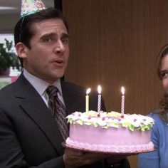 a man standing next to a woman holding a cake with lit candles on top of it