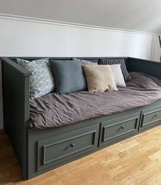 a day bed with drawers underneath it and pillows on the bottom shelf, in front of a window