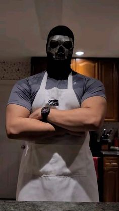 a man in an apron with his arms crossed wearing a black mask and grey t - shirt