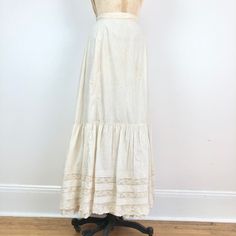 "Antique Victorian white cotton maxi skirt has a 3 layered hem with the a lace inset and pin tuck top layer. The skirt has a gathered back waist. Condition Structurally good condition, missing the back waist closure entirely, and has overall yellowing. There are small stains across the center front hip area and right hip. There are more stains at the back left hip area and center area. Has small splits between the lace inset and cotton throughout the hem, and some small holes in the lace. There' Beige Cotton Skirt With Lace Trim, Elegant Cotton Maxi Skirt For Daywear, Cream Cotton Ruffled Skirt, Fitted Beige Maxi Skirt For Daywear, Fitted Cotton Skirt With Lace Trim, Long Cotton Skirt With Lace Trim, Cotton Skirt With Lace Trim For Daywear, Cream Tiered Skirt For Daywear, Cotton Long Skirt With Lace Trim