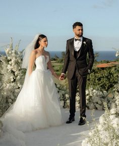 a bride and groom holding hands in front of white flowers at their wedding ceremony with the ocean in the background