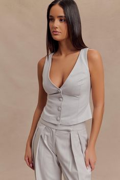 Clean-cut.Elevate your wardrobe with the ASPEN Suiting Vest, a sophisticated piece that seamlessly combines classic tailoring with modern style. Featuring a sleek V neckline and a button front closure, this sleeveless vest offers a streamlined, longline silhouette that flatters every figure. The versatile design makes it an essential addition to any ensemble, perfect for layering over blouses or pairing with the Penelope Pleated High Waisted Pants. Together, these pieces create a polished, cohes Elegant Single-breasted Button-up Vest, Spring Tailored Single-breasted Vest, Elegant V-neck Vest With Buttons, Luxury Tailored Single-breasted Vest, Luxury V-neck Vest With Buttons, Capsule Wardrobe Accessories, Workwear Capsule Wardrobe, Workwear Capsule, Capsule Wardrobe Basics