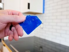 a hand holding a blue piece of plastic in front of a kitchen counter top and sink