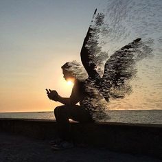 a person sitting on a wall next to the ocean with an angel statue in front of them