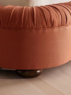 an orange round ottoman sitting on top of a wooden floor next to a white pillow