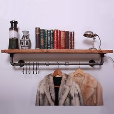 two coats are hanging on a shelf next to some books and other items in front of a white wall