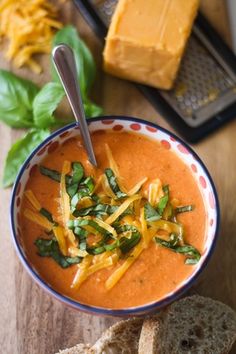 a bowl of soup with cheese and spinach in it on a table next to bread