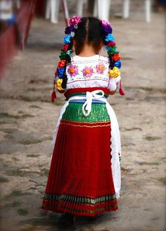 a woman wearing a colorful skirt and flowered headpiece walking down a dirt road