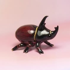 a small black and red beetle on a pink background with gold accents, it's eyes are closed