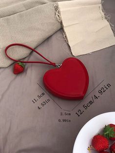 a red heart shaped purse sitting on top of a bed next to a bowl of strawberries