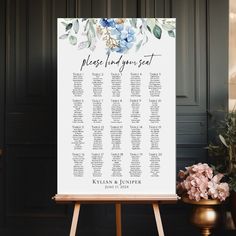 an easel with a seating chart on it next to some flowers and potted plants