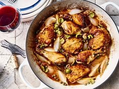 a pan filled with chicken and onions on top of a table next to glasses of wine