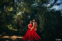 a man and woman standing in front of some trees wearing red dresses with their arms around each other