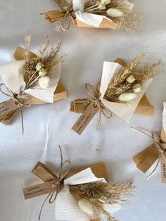 four wrapped gift bags with dried flowers and tags tied to them on a white table cloth