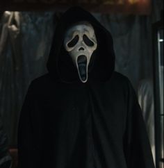 a person in a black hoodie with a white mask on and mouth wide open