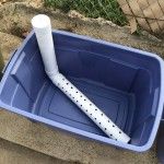 a blue plastic container with a white baseball bat in it sitting on the ground next to a chain link fence