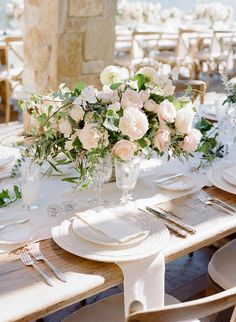 the table is set with white plates and silverware, flowers in vases, and greenery