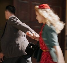 a woman in a red dress is holding the hand of a man in a gray suit