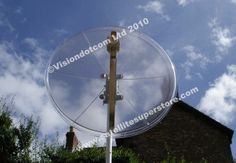 a satellite dish sitting on top of a pole in front of a brick building under a cloudy blue sky