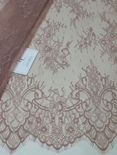 the fabric is pink with white lace on it and has a tag in front of it