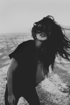 a black and white photo of a woman with her hair blowing in the wind on top of a hill