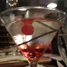 a close up of a wine glass with a cherry on the rim and a drink in it