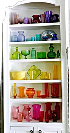 a white shelf filled with lots of colorful glassware