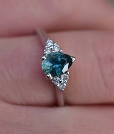 a woman's hand holding a ring with a blue and white diamond