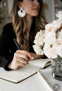 a woman sitting at a table writing on a notebook with flowers in front of her