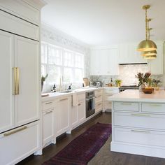 a large kitchen with white cabinets and gold accents on the counters, along with an area rug that matches the hardwood flooring