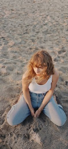 a woman sitting in the sand with her hands on her knees and looking at the camera