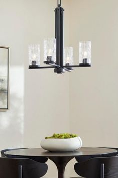 a dining room table and chairs with a bowl of food on it in front of the chandelier